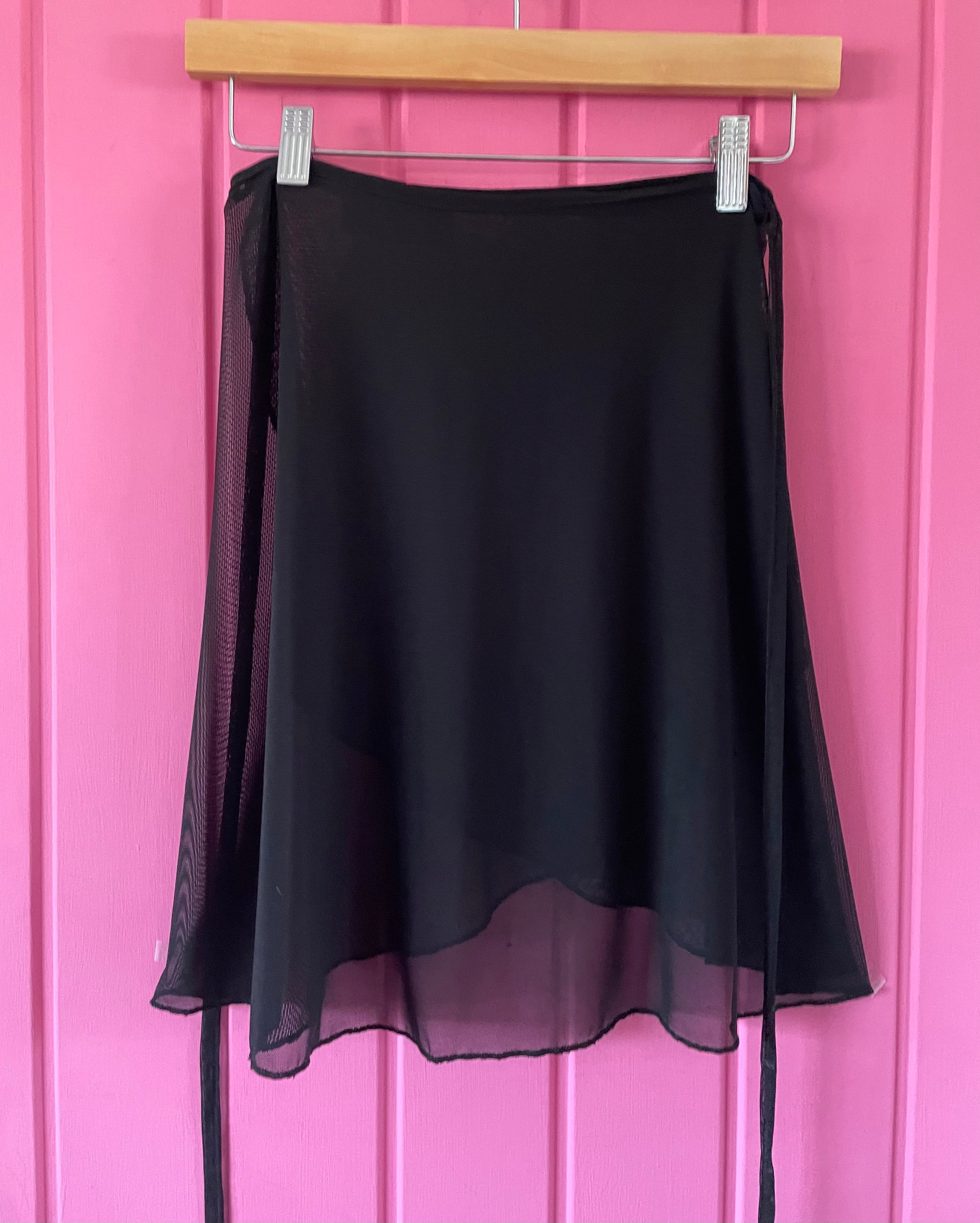 Black sheer skirt on a hanger against a pink background